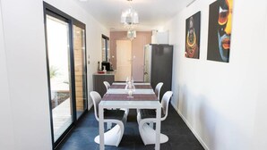 Een moderne eetruimte met een tafel met glazen blad, witte stoelen en een kroonluchter.