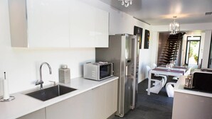 Een moderne keuken met witte kasten, roestvrijstalen apparatuur en een eethoek met een trap naar een ander niveau.