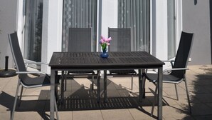 Un edificio de dos pisos con un balcón, ventanas amplias y una mesa con sillas afuera.