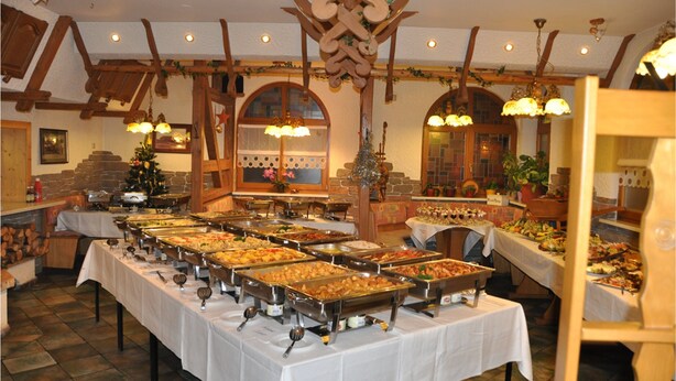 Ein reichhaltiges Buffet mit mehreren Speiseauslagen, Holzbalken und Kristalllüstern in rustikalem Ambiente.