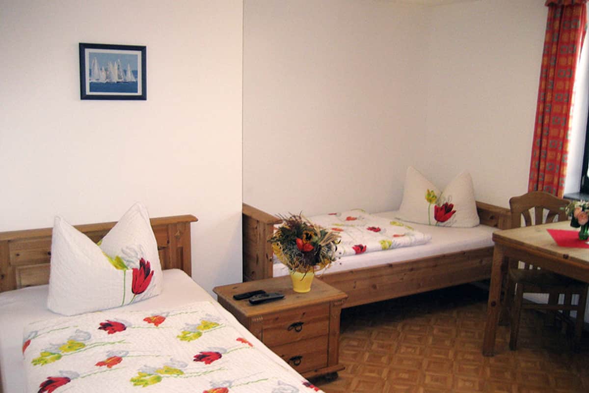 Een kamer met twee éénpersoonsbedden, een nachtkastje van hout met een bloevas, een houten tafel en een stoel.