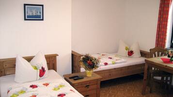 Una habitación con dos camas individuales, una mesita de noche de madera con un florero y una silla. También hay una mesa de madera.
