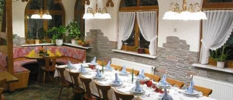 A dining area with tables set for a meal, wooden chairs, and a stone wall.