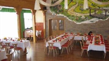 A dining area with multiple tables set for service, a mural on the wall, and wooden flooring.