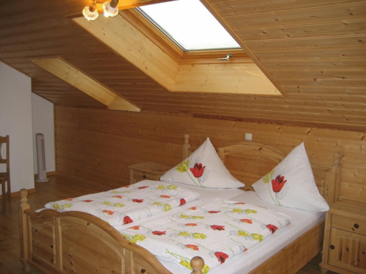 A wooden room with a sloped ceiling, a bed with floral bedding, and a skylight.