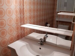 Une salle de bain avec un lavabo blanc, un miroir et des toilettes.