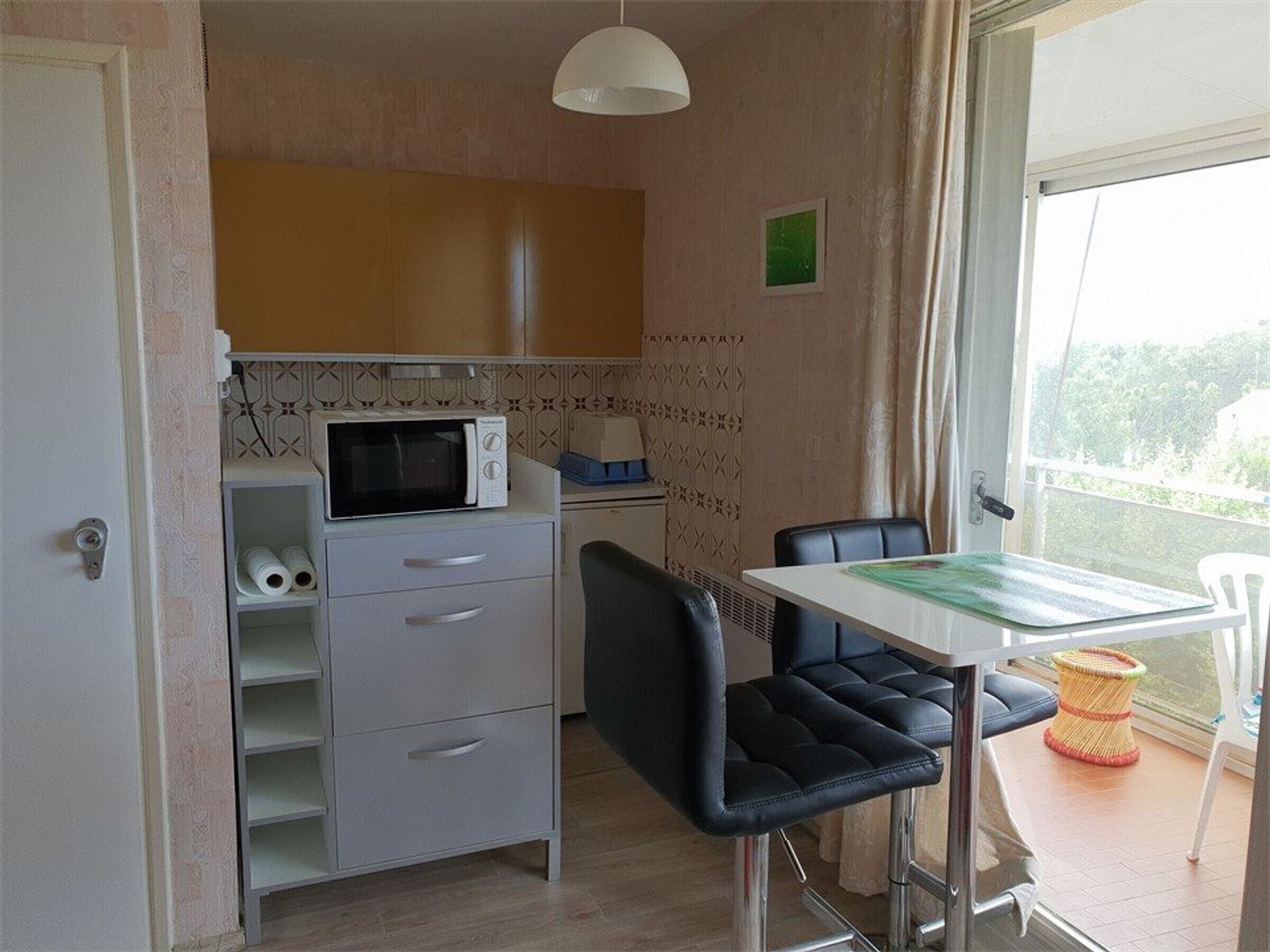 A compact kitchen with a microwave, a small refrigerator, and a dining area with a table and chairs.