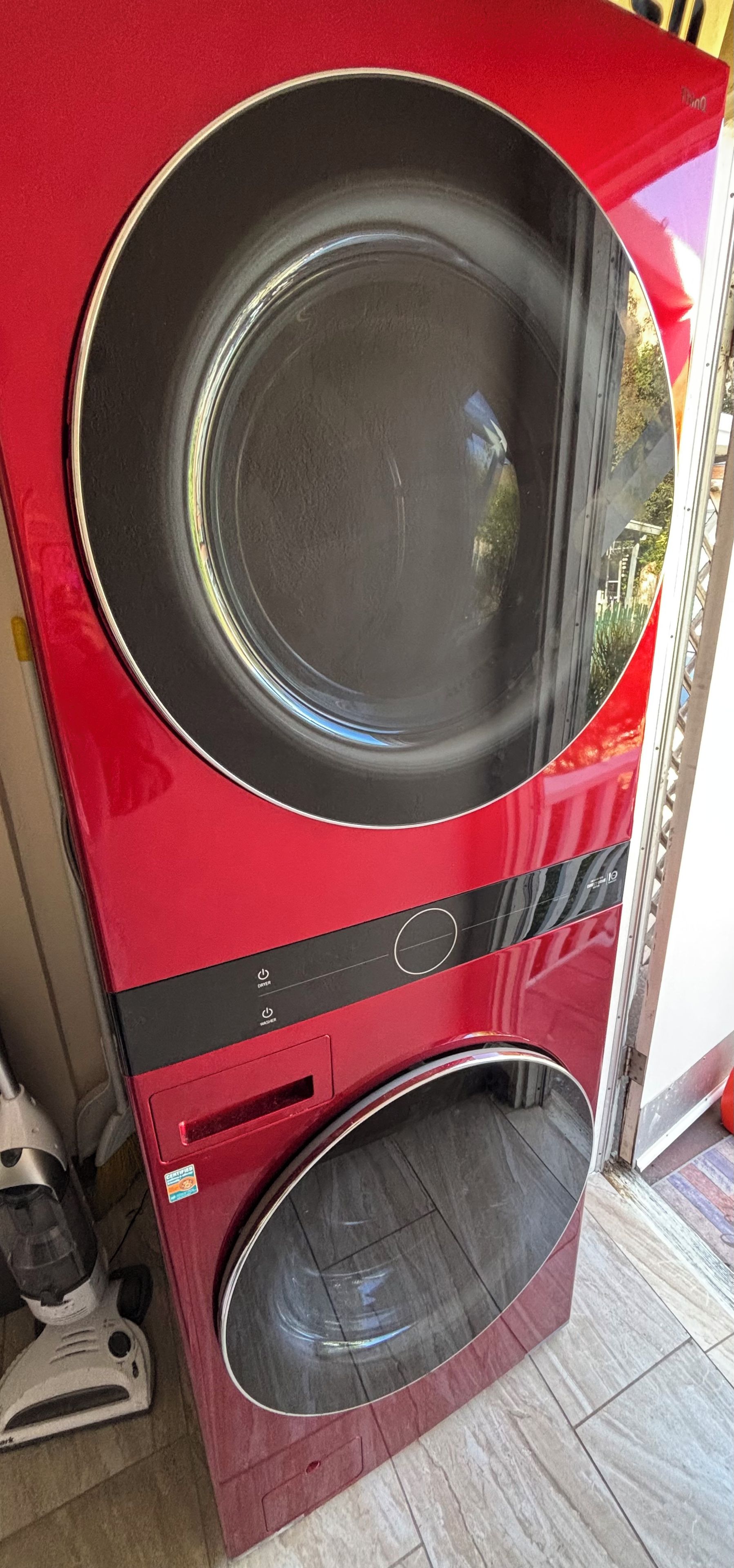 A red washing machine with a front-loading door, a control panel with buttons, and a small sticker on the side.
