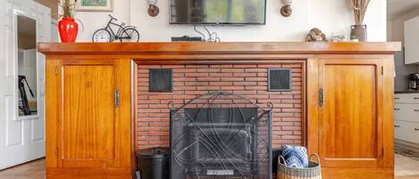 A kitchen with a brick fireplace, wooden cabinets, a TV mounted above, and a red vase on the counter.