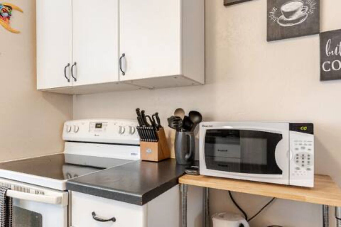 A kitchen with white cabinets, a microwave, and a stove. There are utensils on the counter and a coffee cup on the wall.