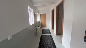 Un pasillo estrecho con pared blanca, una puerta de madera y un felpudo blanco y negro en el suelo.