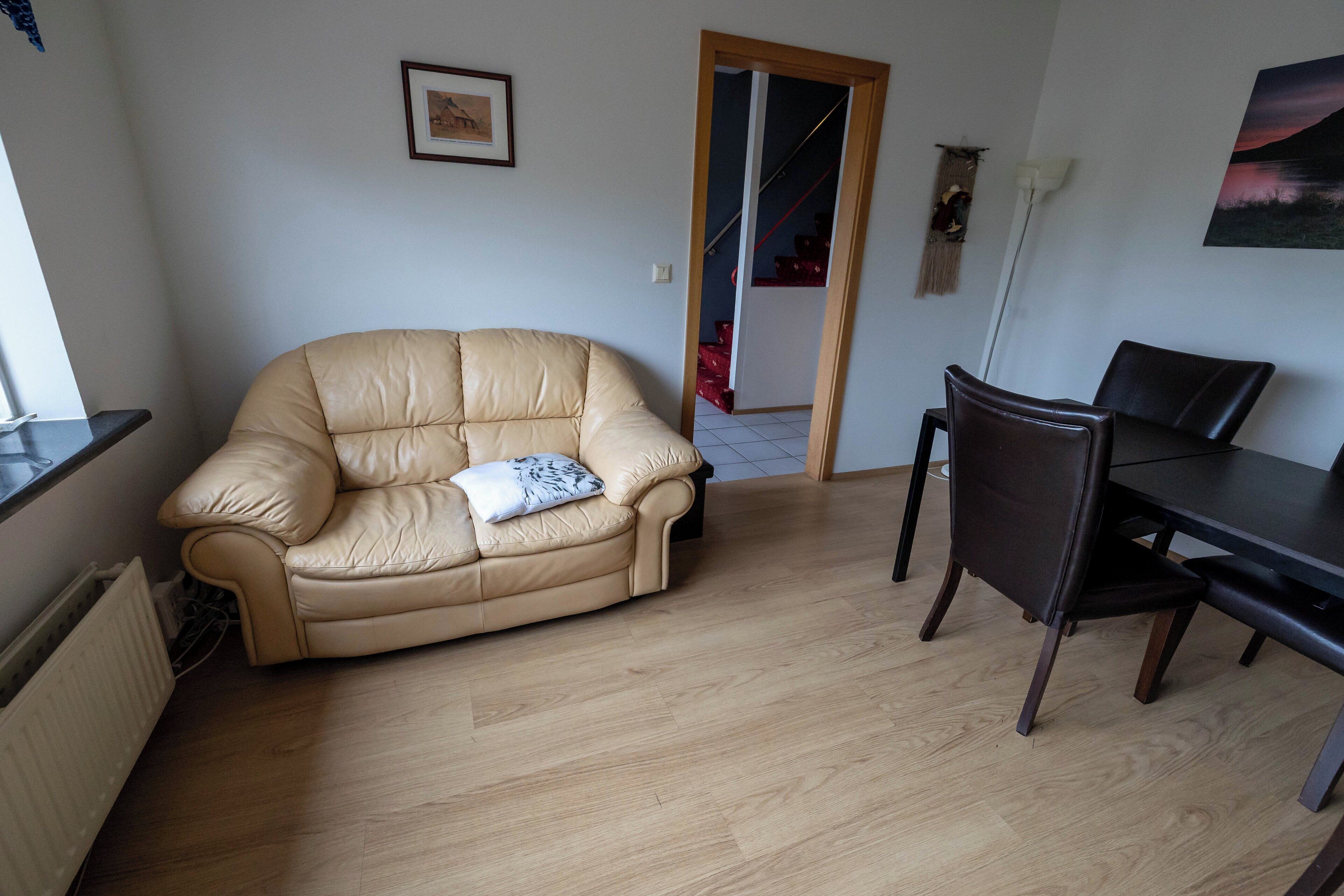 Uma sala de estar com um sofá bege, uma mesa de jantar com cadeiras, um radiador e um quadro na parede.