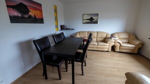 Una sala de estar con una mesa de comedor y sillas, un sofá color beige y dos obras de arte colgadas en la pared.