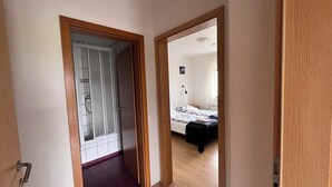 A hallway leading to a bedroom with a bed, a nightstand, and a window.