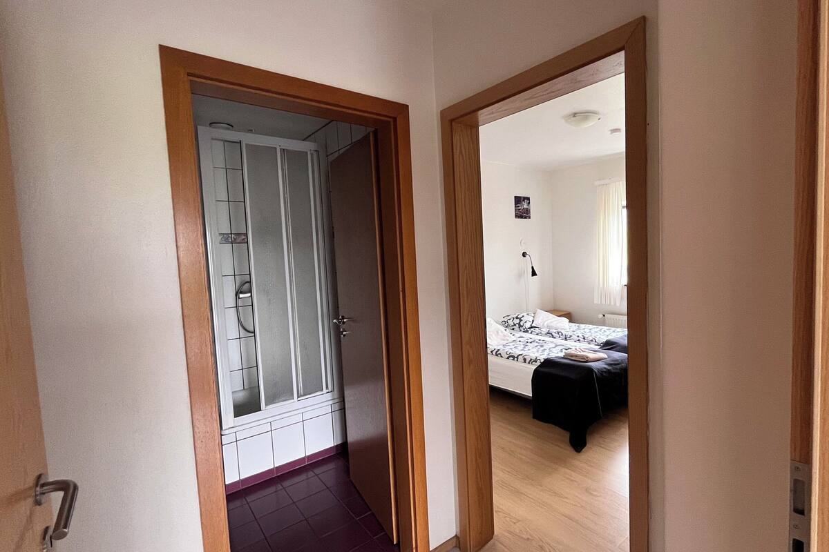 Un pasillo que conduce a un dormitorio con una cama, una mesita de noche y una ventana.