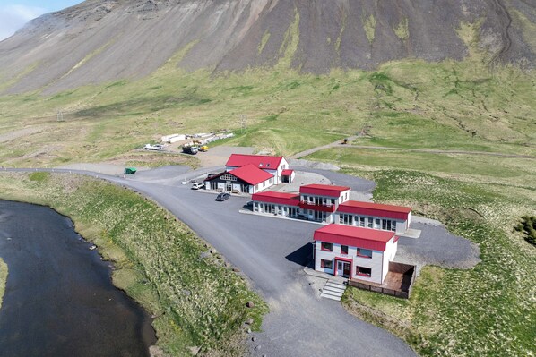 A small hotel with a red roof, located near a body of water and a mountainous backdrop. - Grund guesthouse (Grundarfjörður)