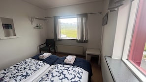 Habitación de hotel con dos camas, una silla, un escritorio, una ventana con vistas a montañas y un radiador.
