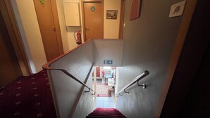 Una escalera con barandillas, un extintor y un cartel que indica la dirección de la salida.