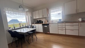 Cocina con vistas a una montaña y un lago, armarios de madera, lavavajillas y un comedor con sillas.