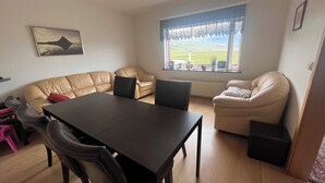 A living room with a beige sofa, a black dining table, and a window with a view of a green landscape.