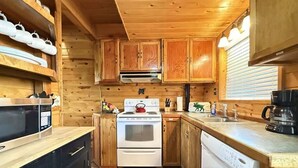 Een kleine keuken met houten kastjes, een magnetron, fornuis en vaatwasser.