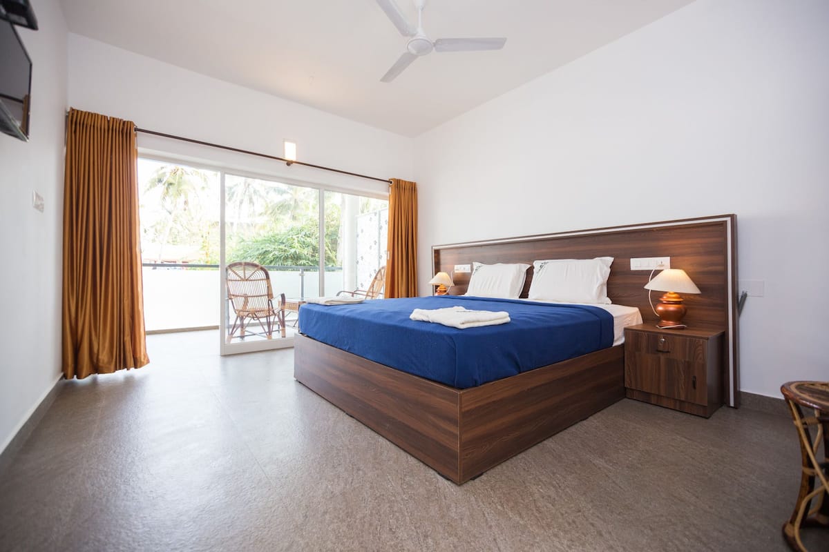 Un dormitorio con una cama grande, una mesita de noche, una lámpara, una silla y vistas al exterior a través de una puerta corredera.