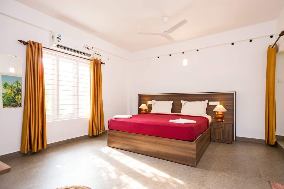 Una habitación de hotel con una cama grande, un ventilador de techo, un equipo de aire acondicionado y una mesita de noche con lámpara.
