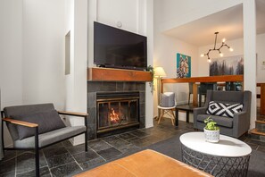 Een moderne woonkamer met een open haard, een flatscreen televisie en een eethoek met een kroonluchter.