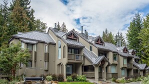 Un immeuble résidentiel moderne à plusieurs étages, doté d’une conception symétrique, de balcons, de grandes fenêtres et d’un espace jardin bien entretenu.