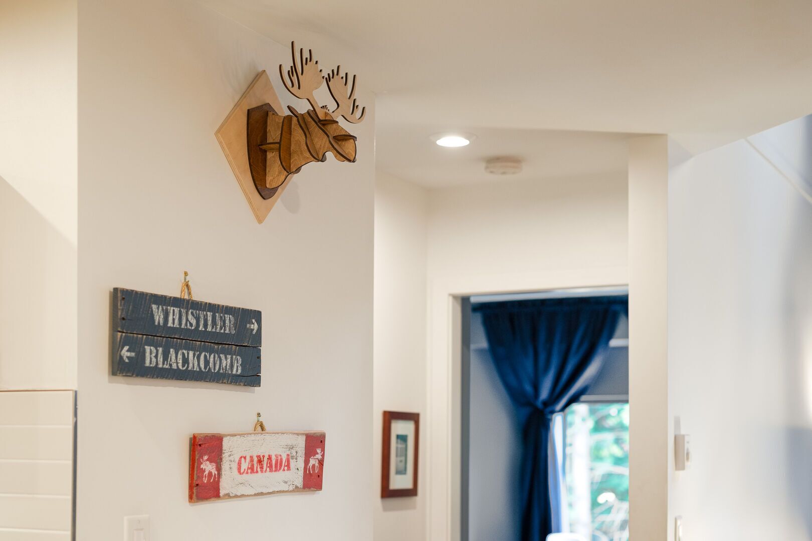 Un couloir avec un panneau en bois indiquant les directions vers les stations de ski de Whistler et de Blackcomb, ainsi qu’un autre panneau représentant un orignal et le mot « Canada ».