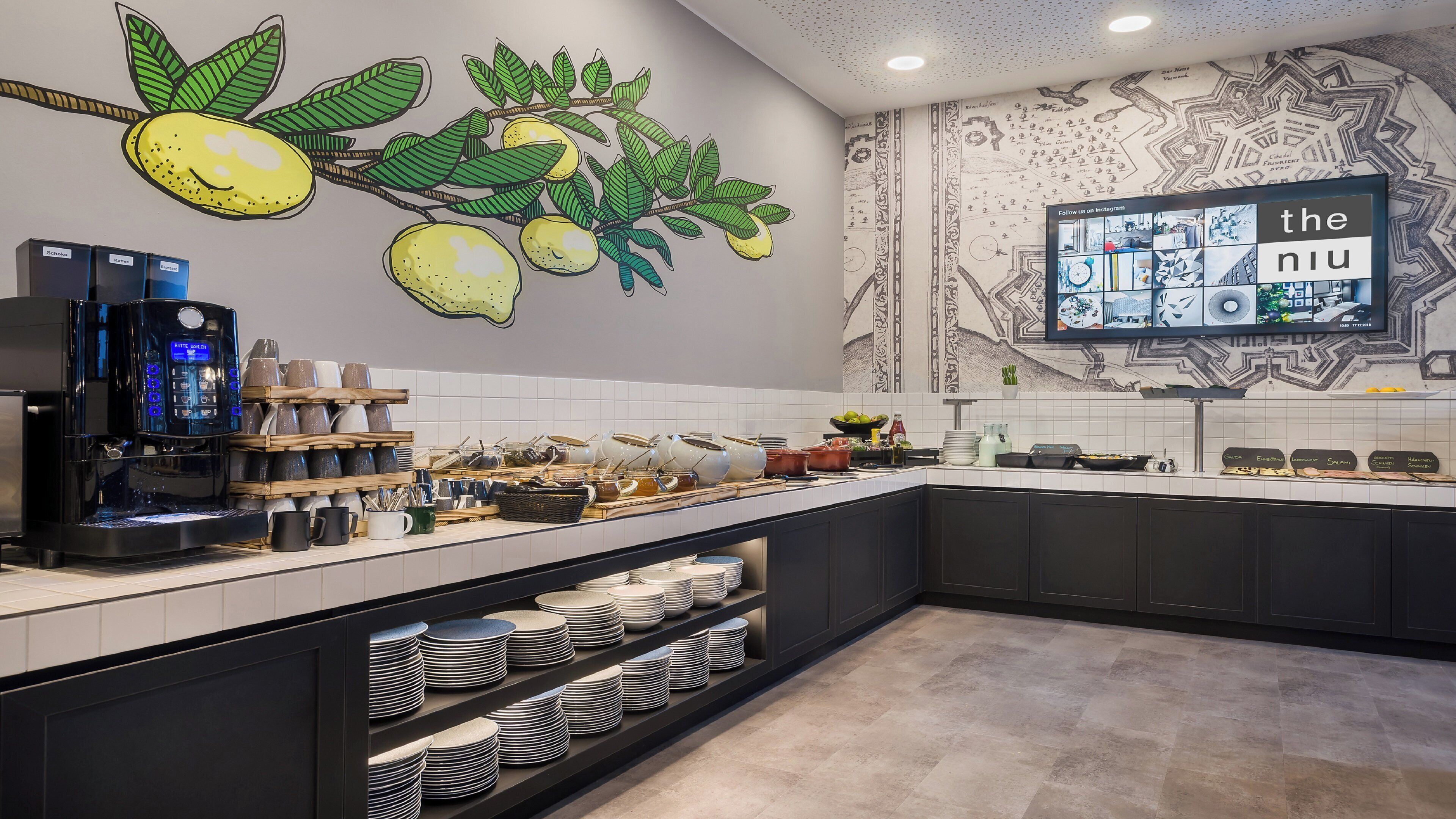 Une cuisine moderne équipée d’une machine à café, ornée d’une fresque murale et dotée d’un téléviseur à écran plat affichant une application de réseau social.
