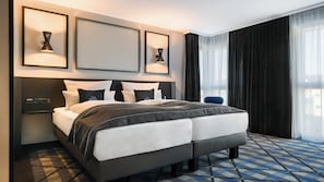 Habitación de hotel moderna con una cama grande, lámparas de noche, un televisor de pantalla plana y vistas de la ciudad a través de cortinas translúcidas.