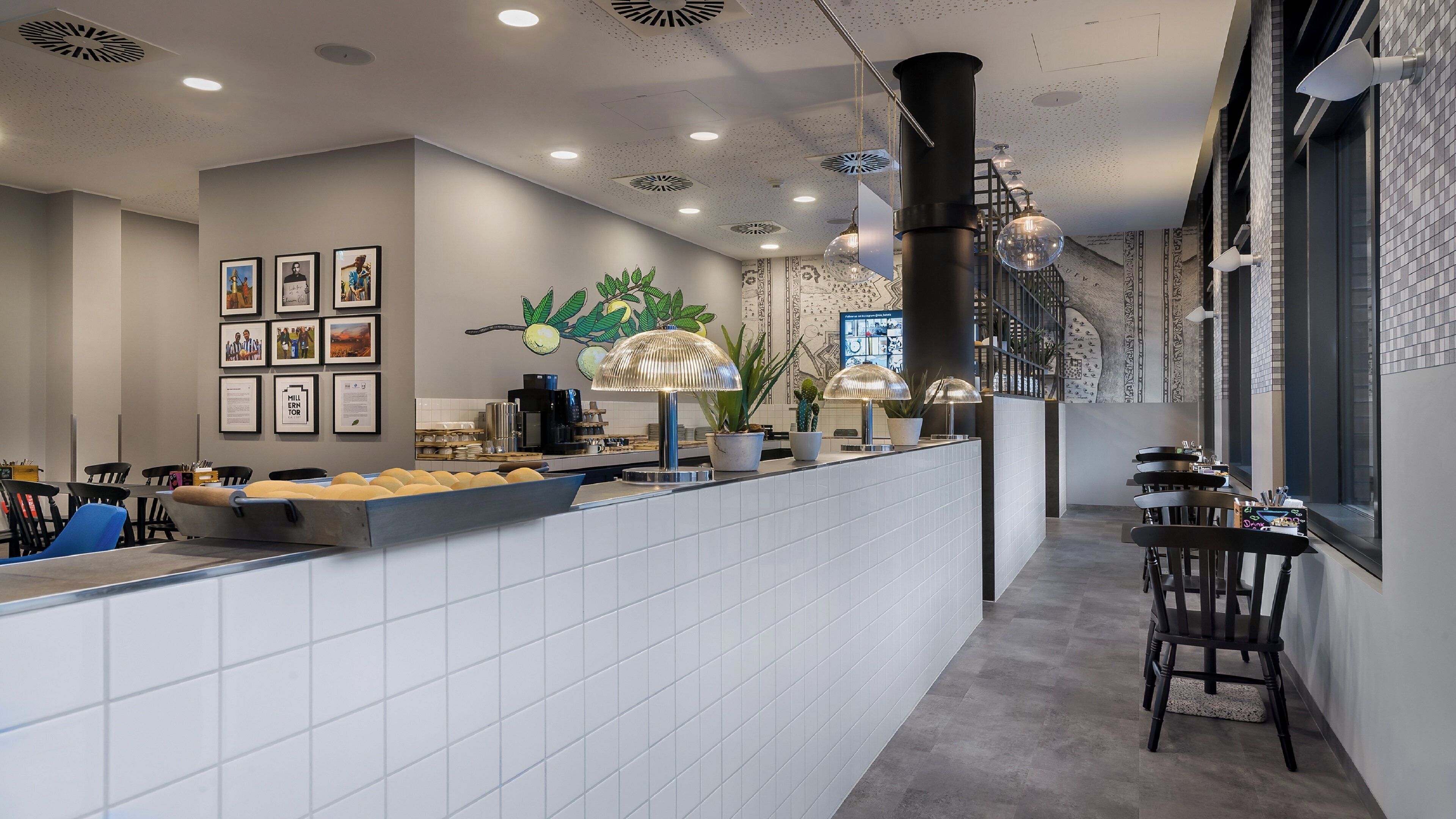 Interior de una cafetería moderna con mostrador, zona de estar y detalles decorativos como plantas y cuadros.