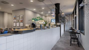Interior de una cafetería moderna con mostrador, zona de estar y detalles decorativos como plantas y cuadros.