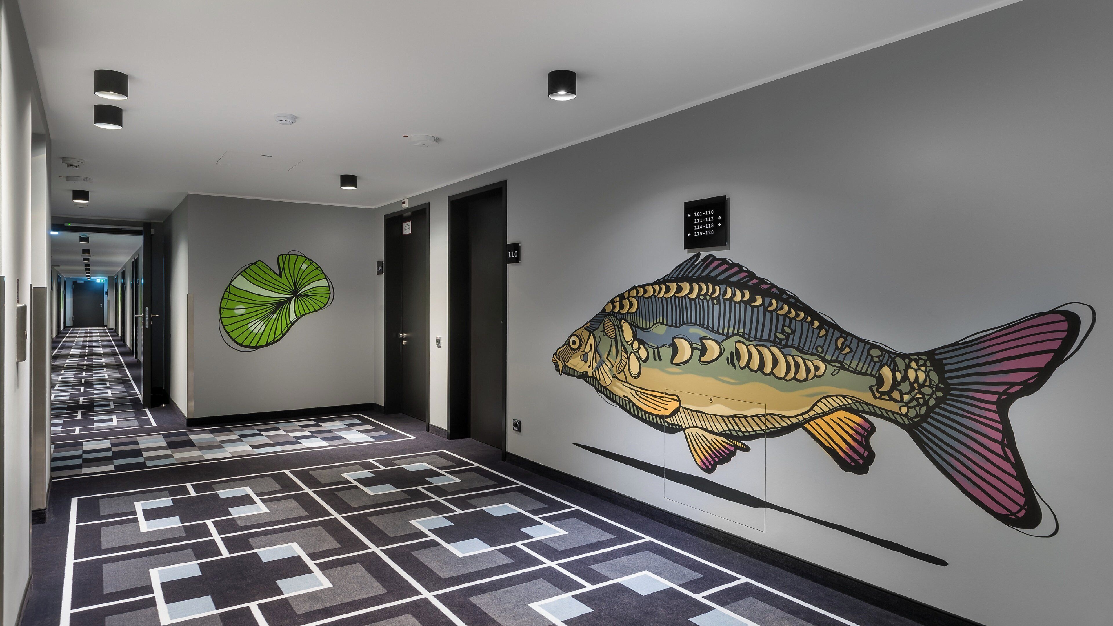 A hallway with a checkered floor, a large fish mural, and a door with a number sign.