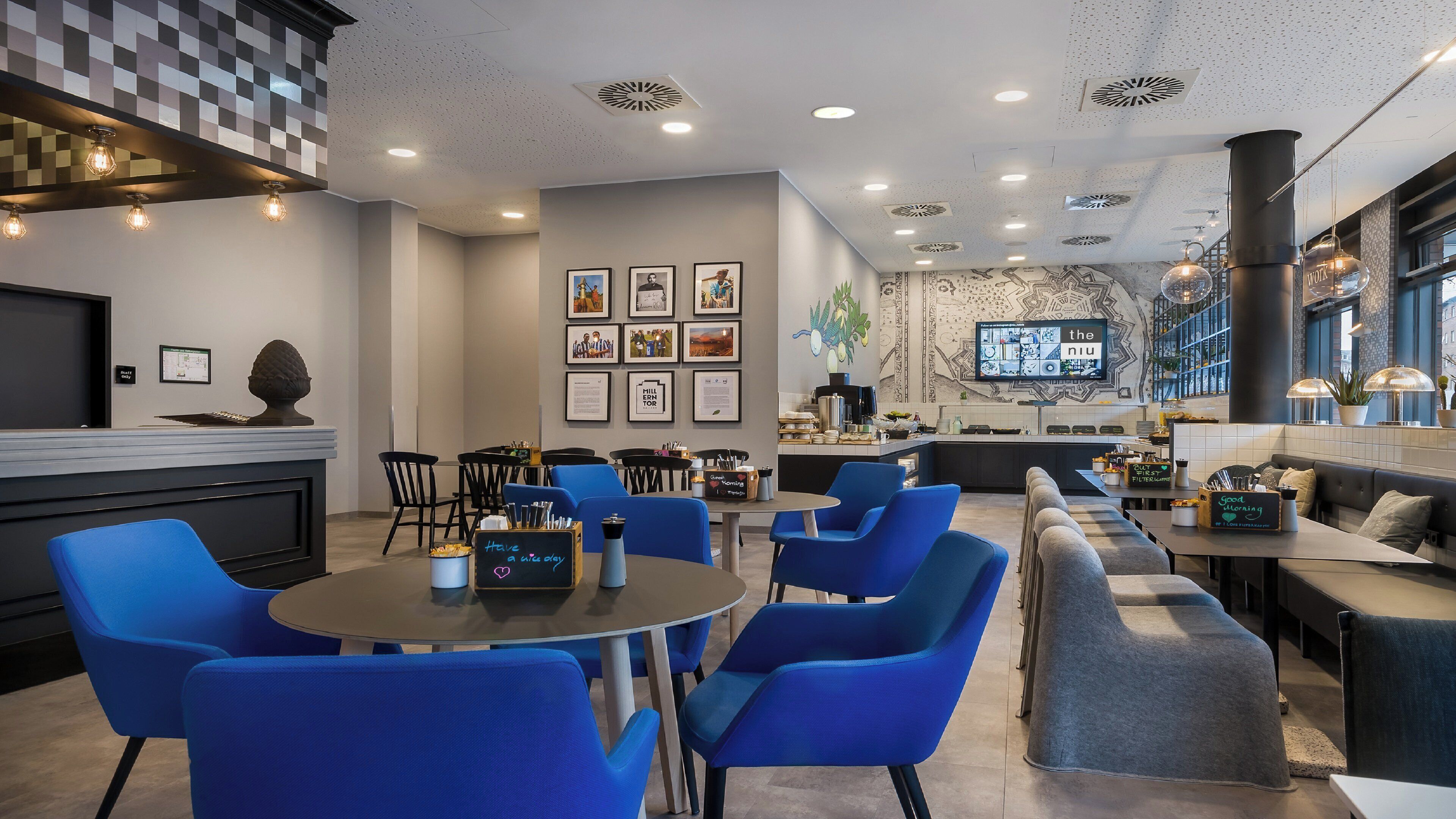 Un interior moderno con mesas redondas, sillas azules, una zona de bar y una pantalla de televisión que muestra un menú.