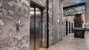 Un pasillo interior con paredes con diseño, un ascensor y un mostrador de recepción.