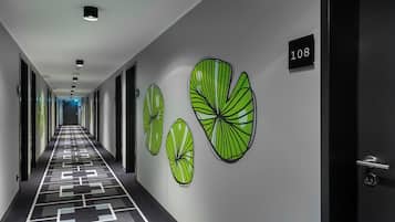 Ein Hotelkorridor mit einem gemusterten Boden, Wandkunst mit Blättern und einer Tür mit der Nummer 108.