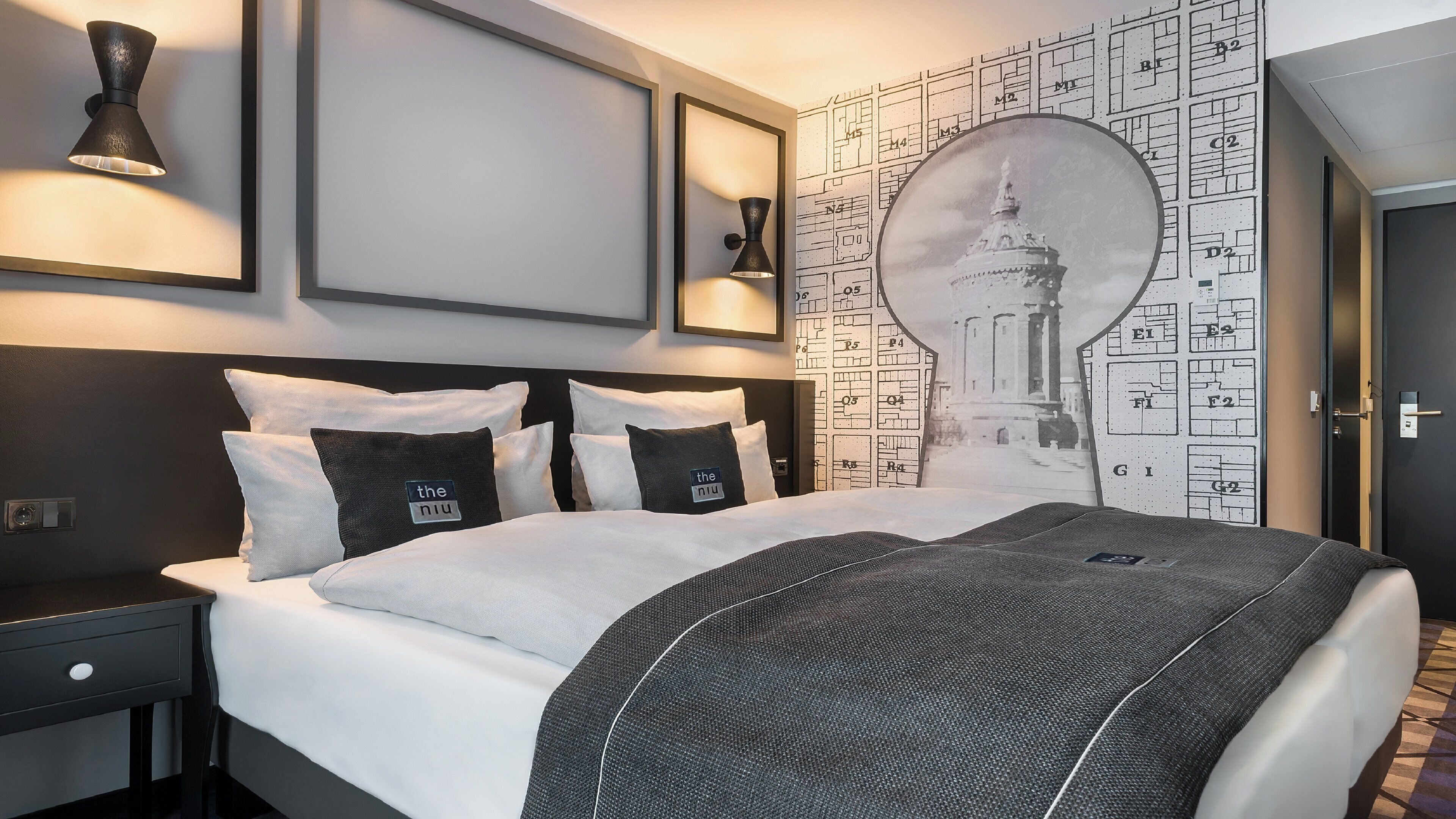 Una camera d'albergo moderna con un letto grande, un comodino, una lampada a parete e una parete con un motivo a mappa.