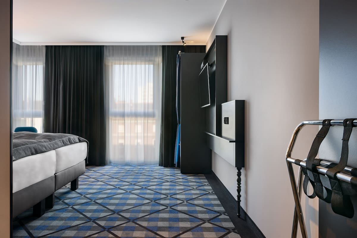 Una habitación de hotel con cama, ducha, televisor montado en la pared y piso estampado.