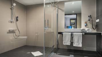 A modern bathroom with a glass-enclosed shower, a toilet, and a sink with two towels.