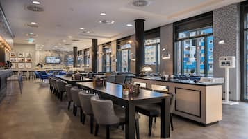 A modern restaurant with a long counter, multiple seating options, and large windows offering city views.