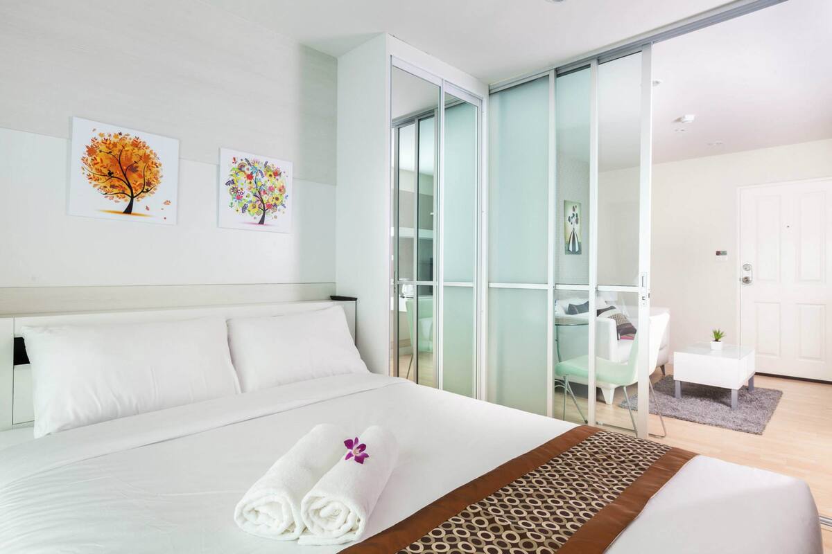 A modern hotel room with a large bed, a glass door leading to a balcony, and two wall-mounted artworks.