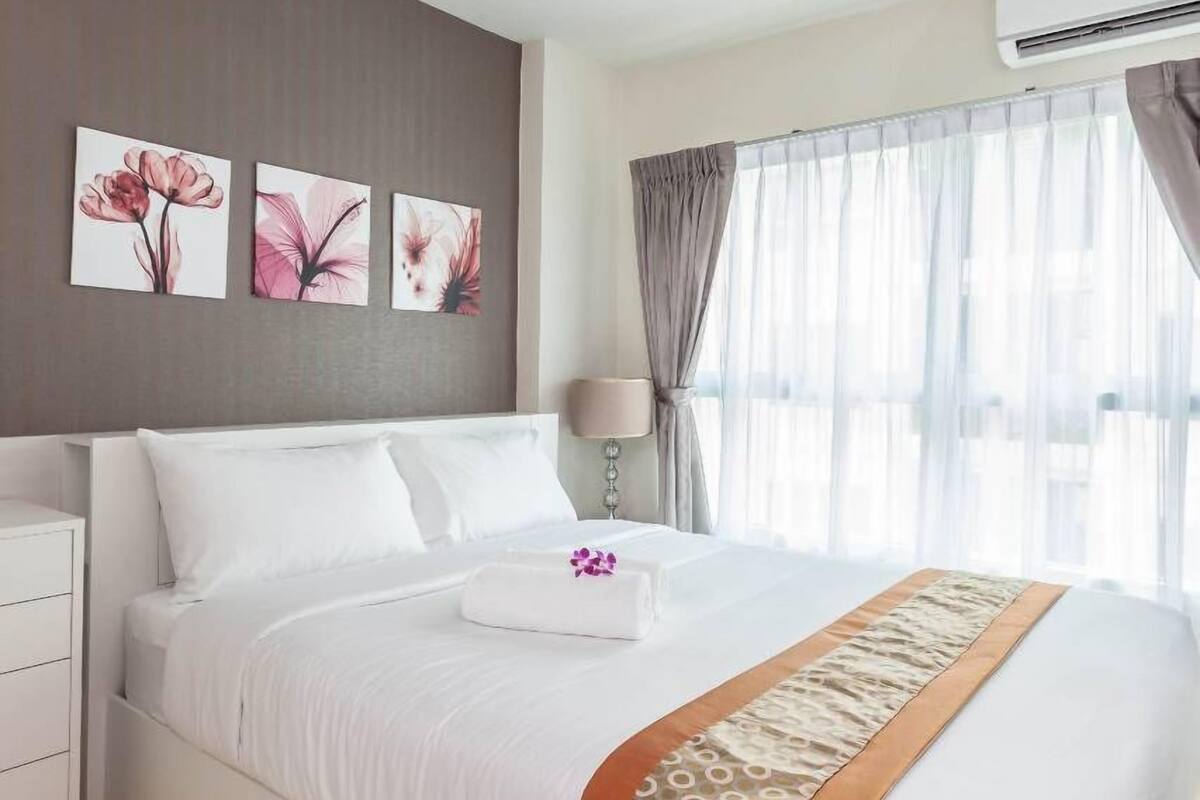 A hotel room with a large bed, a bedside table, a lamp, and three floral paintings on the wall.