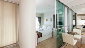 A modern hotel room with a bed, a glass partition, a dining area with a table and chairs, and a view of the room. - The Cube Residence Government Complex Laksi (Bangkok)