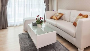 A modern living room with a white sofa, a glass coffee table, and a grey rug. - The Cube Residence Government Complex Laksi (Bangkok)