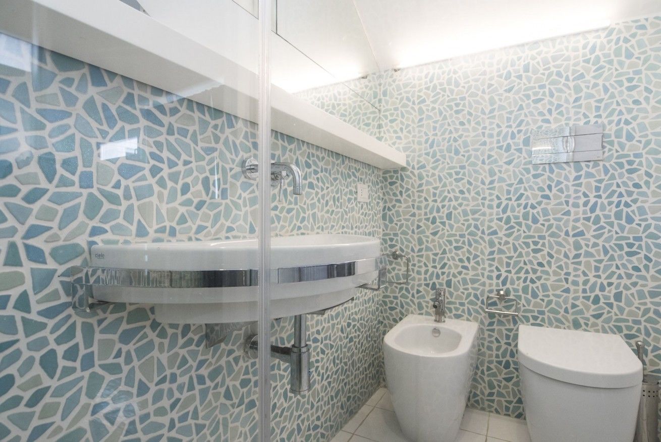 A bathroom with mosaic tile walls, a white sink, a bidet, and a toilet.