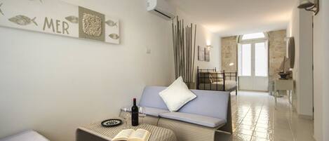 Una sala de estar moderna con un sofá, una mesita de centro con un libro y vino, y una pared con un letrero que dice 'MER'.