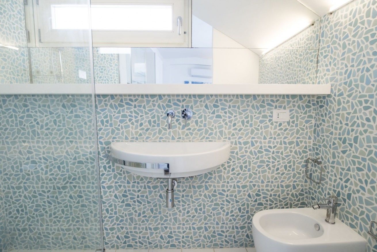 Un baño con pared de mosaicos, un lavamanos blanco y un bidé.