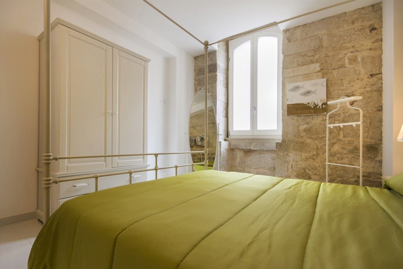A bedroom with a bed, a wardrobe, a window, and a stone wall.